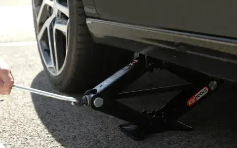 Utilisation d'un cric en ciseaux pour trouver le bon point de levage voiture. La roue est visible.