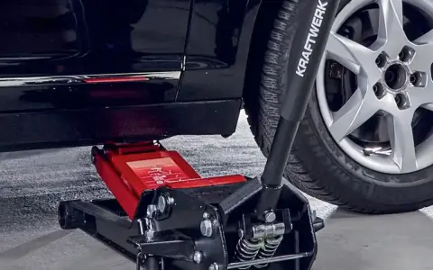 Un cric hydraulique rouge est positionné pour soulever une voiture. Il est essentiel de savoir ou placer le cric sous la voiture pour un changement de roue sûr.