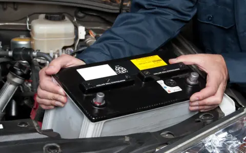 Maintenant, le démontage de la batterie de voiture est en cours. Les mains d'un mécanicien retirent la batterie noire du compartiment moteur.