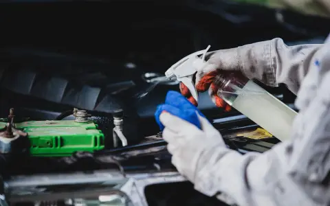 Gants et chiffon bleu pour comment nettoyer un moteur de voiture plein d'huile. Vaporisation d'un produit sur le moteur.