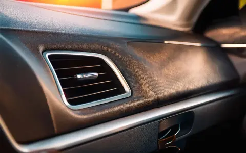 Tableau de bord d'une voiture avec une grille de ventilation chromée. La question "combien de temps dure une clim voiture" résonne dans l'habitacle climatisé.