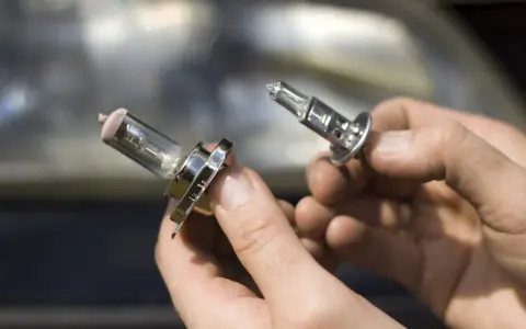 Deux ampoules de feu de croisement voiture sont tenues dans des mains. L'une est déjà retirée, l'autre est sur le point de l'être.
