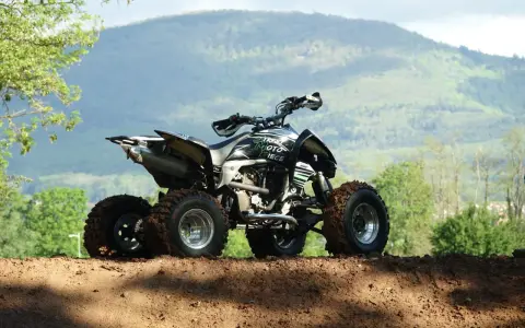 Quad tout-terrain, prêt pour son contrôle technique, avec des pneus boueux et un paysage montagneux en arrière-plan.