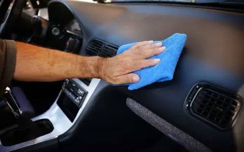 Main d'homme nettoyant le tableau de bord d'une voiture avec un chiffon bleu. Un nettoyant plastique voiture fait maison pour un intérieur impeccable.
