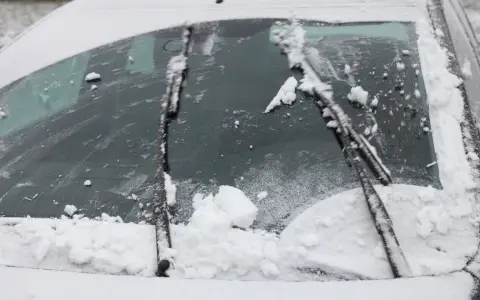 Pare-brise enneigé, un essuie-glace bloqué au milieu, prêt à dégager la vue.