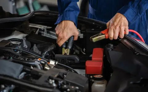 Mains de mécanicien effectuant le branchement batterie voiture avec des câbles de démarrage.