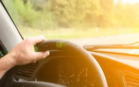 Main d'un conducteur tenant le volant d'une voiture qui tremble au point mort, sous un soleil éclatant.