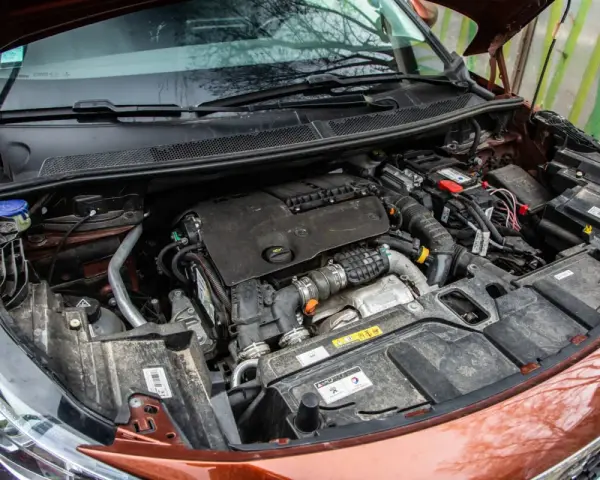 Vue rapprochée du moteur d'une voiture, prêt pour un nettoyage. On voit le bloc moteur, la batterie et divers composants.
