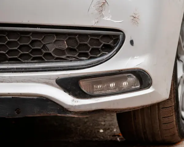 Pare-chocs avant d'une voiture blanche avec des éraflures et des éclats de peinture. Une méthode pour redresser carrosserie eau chaude pourrait aider à réparer ces dommages.