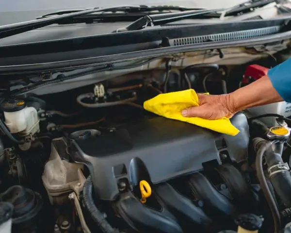 Main d'un mécanicien nettoyant le moteur d'une voiture avec un chiffon jaune, comme s'il utilisait un dégraissant moteur fait maison.