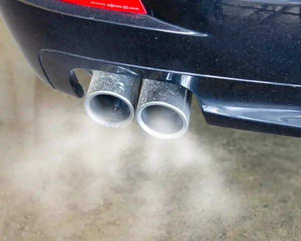 Double sortie d'échappement d'une voiture émettant de la fumée. Une odeur d'échappement dans l'habitacle peut être un signe de problème.