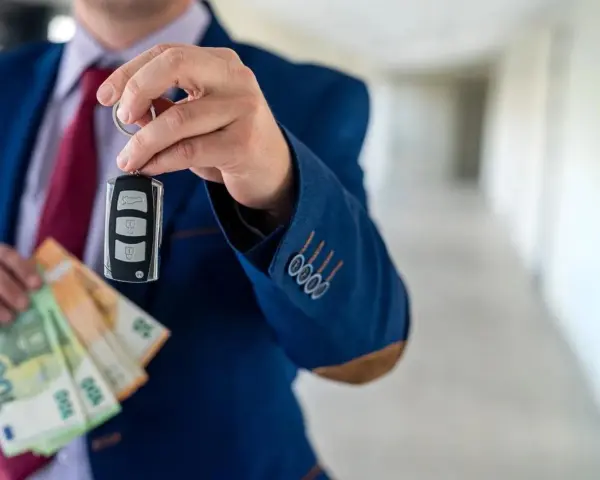 Un homme en costume tient une clé de voiture et des billets en euros. La question est : peut-on payer une voiture en liquide ?