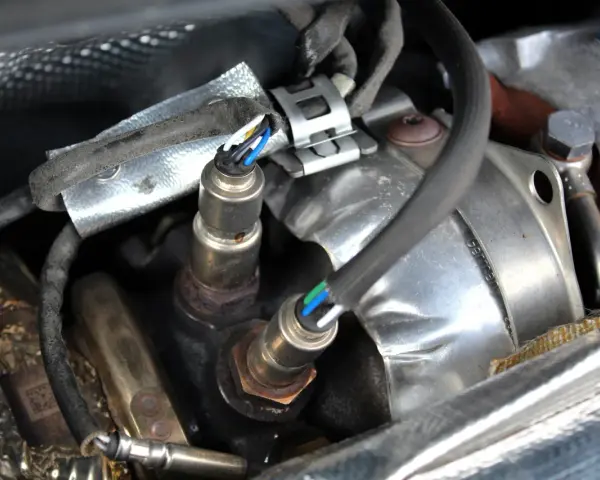 Deux sondes lambda, câblage visible, dans un compartiment moteur. Un nettoyage pourrait améliorer leur efficacité.