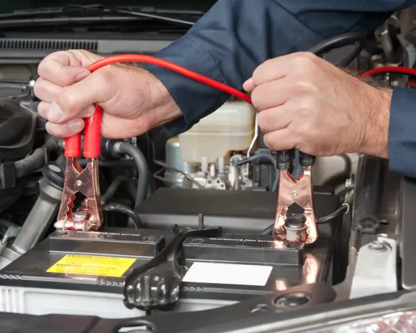 Mains pour recharger batterie voiture avec des câbles de démarrage. Les pinces rouges sont connectées à la batterie.