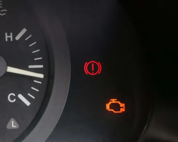 Tableau de bord d'une voiture avec le voyant moteur allumé, signalant un problème. Le voyant d'alerte de freinage est également visible.