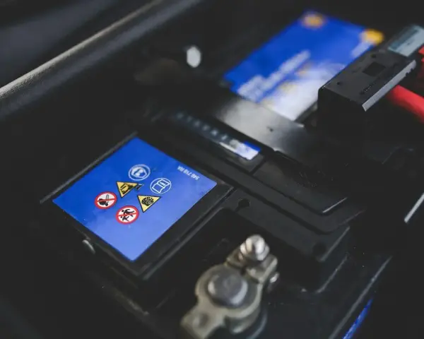 Gros plan sur une batterie de voiture, avec des symboles de sécurité et des câbles rouges. L'image évoque la durée de vie batterie voiture.