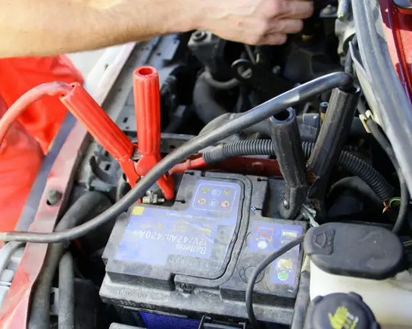 Comment utiliser un booster de batterie : des câbles rouges et noirs sont connectés à une batterie de voiture pour la démarrer.