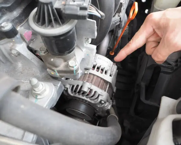 Main d'un mécanicien pointant vers l'alternateur pour tester un régulateur de tension dans un compartiment moteur.