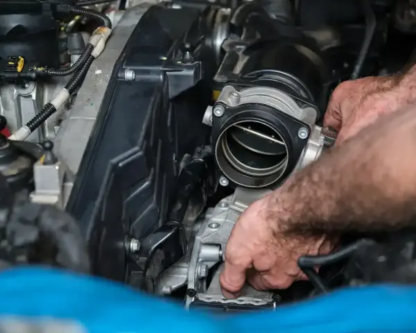Mains d'un mécanicien travaillant sur un moteur, possiblement pour diagnostiquer un débitmètre d'air défectueux symptôme.