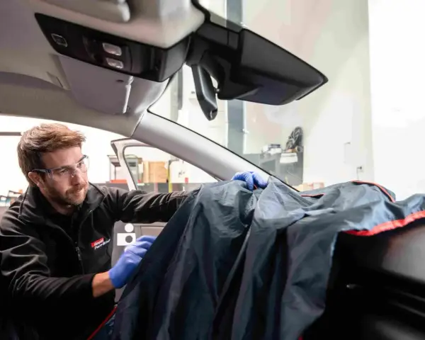 Un technicien en lunettes de protection utilise une housse pour protéger le tableau de bord lors d'une intervention sur la commande de désembuage.