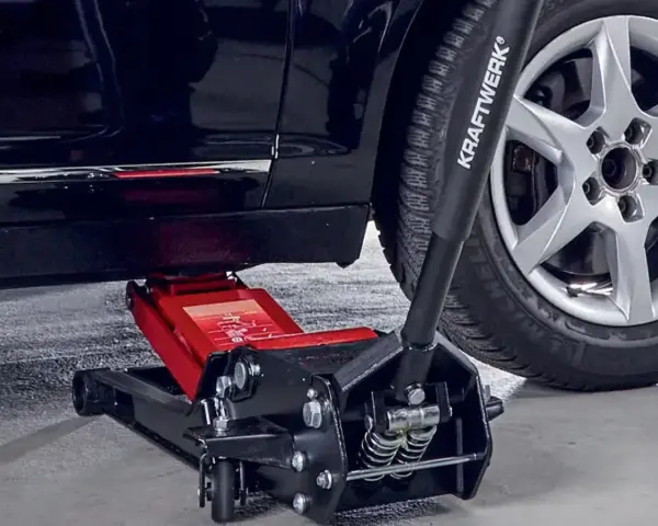 Un cric hydraulique rouge est positionné pour soulever une voiture. Il est essentiel de savoir ou placer le cric sous la voiture pour un changement de roue sûr.