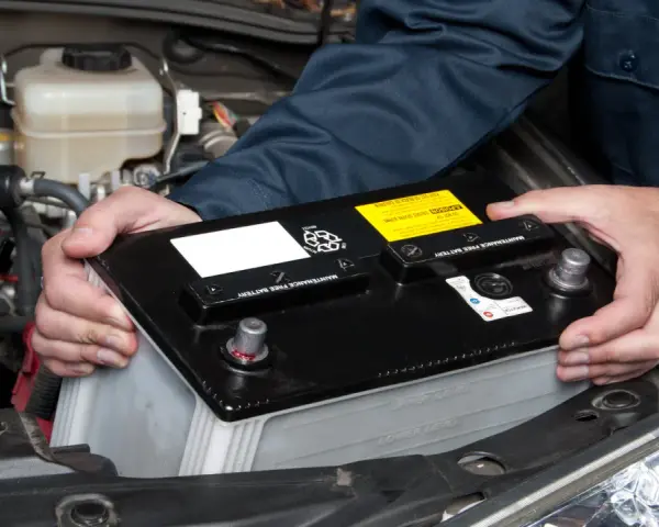 Maintenant, le démontage de la batterie de voiture est en cours. Les mains d'un mécanicien retirent la batterie noire du compartiment moteur.