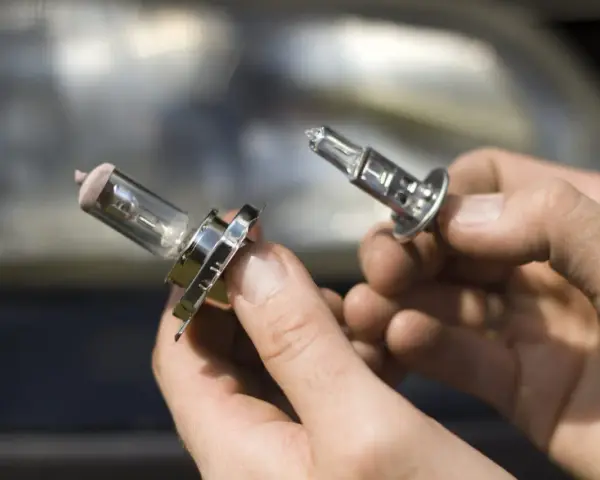 Deux ampoules de feu de croisement voiture sont tenues dans des mains. L'une est déjà retirée, l'autre est sur le point de l'être.