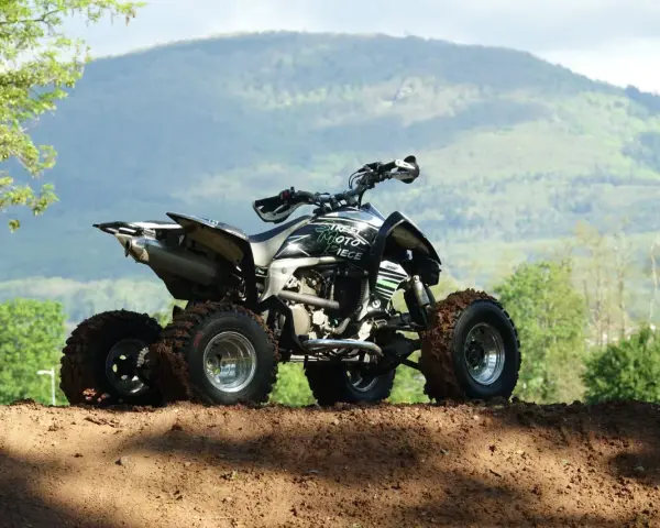 Quad tout-terrain, prêt pour son contrôle technique, avec des pneus boueux et un paysage montagneux en arrière-plan.