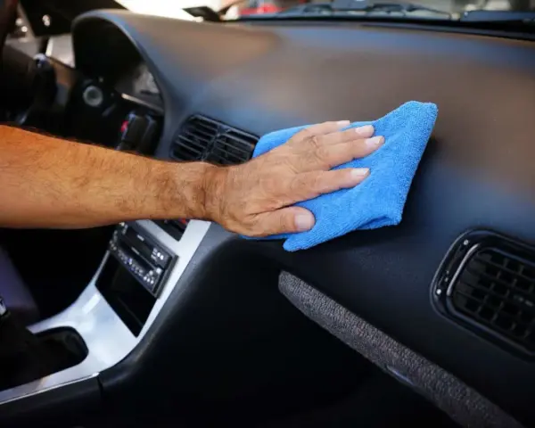 Main d'homme nettoyant le tableau de bord d'une voiture avec un chiffon bleu. Un nettoyant plastique voiture fait maison pour un intérieur impeccable.