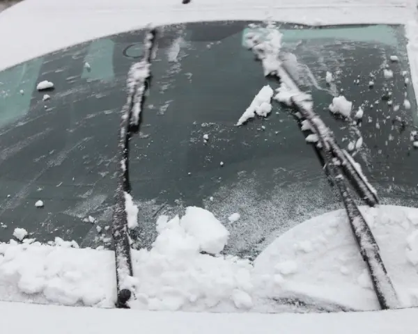 Pare-brise enneigé, un essuie-glace bloqué au milieu, prêt à dégager la vue.