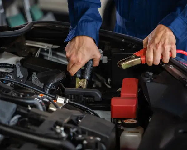 Mains de mécanicien effectuant le branchement batterie voiture avec des câbles de démarrage.