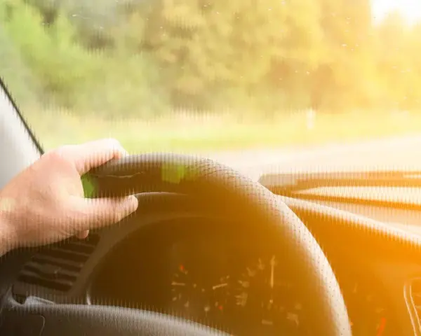 Main d'un conducteur tenant le volant d'une voiture qui tremble au point mort, sous un soleil éclatant.