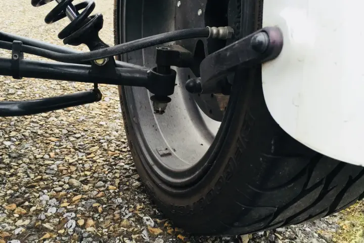 Gros pneu de véhicule sur un chemin de gravier. Le système de suspension et de direction est visible. J'espère que mes pneus font du bruit quand je roule, car cela pourrait indiquer un problème.