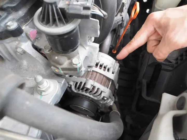 Main d'un mécanicien pointant vers l'alternateur pour tester un régulateur de tension dans un compartiment moteur.
