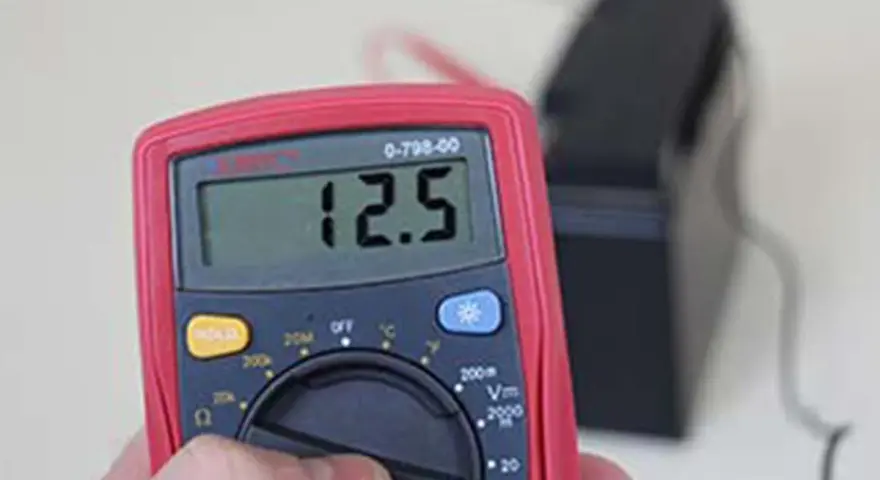 Multimètre affichant 12.5V, indiquant une batterie déchargée ou morte.
