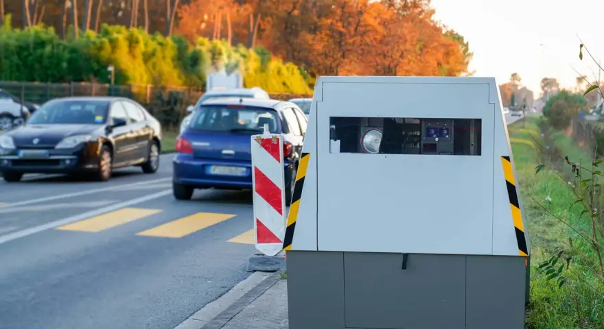 Un radar mobile de voiture surveille la route. Des voitures passent devant, dans un décor automnal.