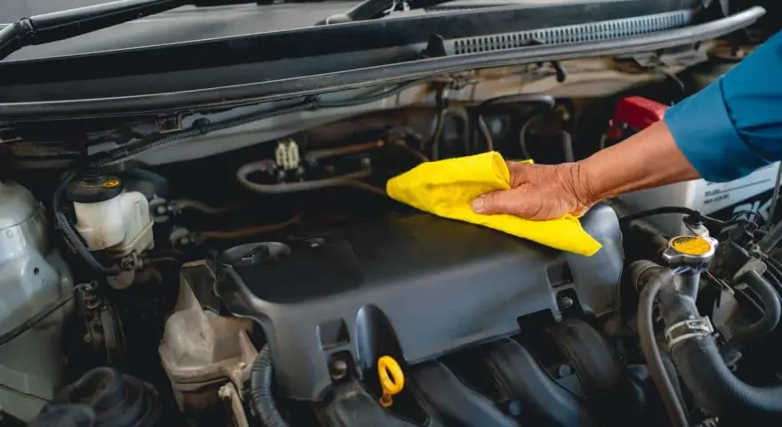 Main d'un mécanicien nettoyant le moteur d'une voiture avec un chiffon jaune, comme s'il utilisait un dégraissant moteur fait maison.