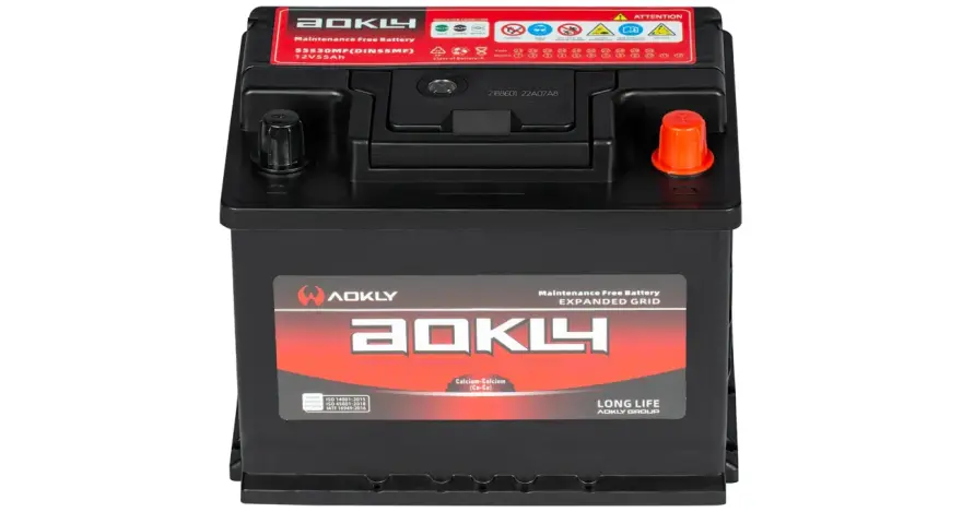 Une batterie AOKLY noire, 12V 55Ah, avec des étiquettes rouges et blanches indiquant "Maintenance Free Battery" et des symboles d'attention.