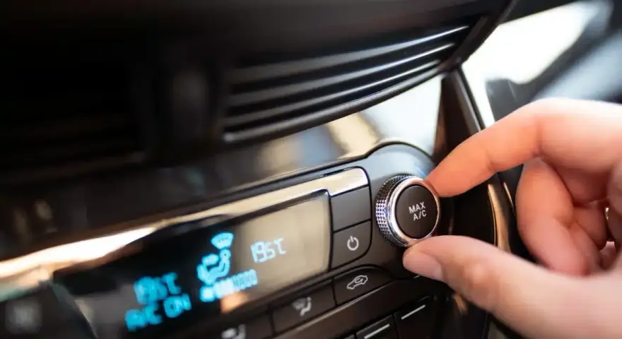 Main de conducteur ajustant le bouton "MAX A/C" sur le tableau de bord. Faut-il laisser la climatisation voiture en permanence ?