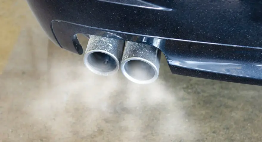 Double sortie d'échappement d'une voiture émettant de la fumée. Une odeur d'échappement dans l'habitacle peut être un signe de problème.