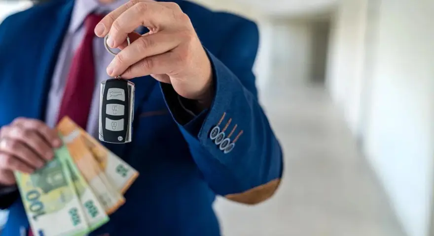 Un homme en costume tient une clé de voiture et des billets en euros. La question est : peut-on payer une voiture en liquide ?