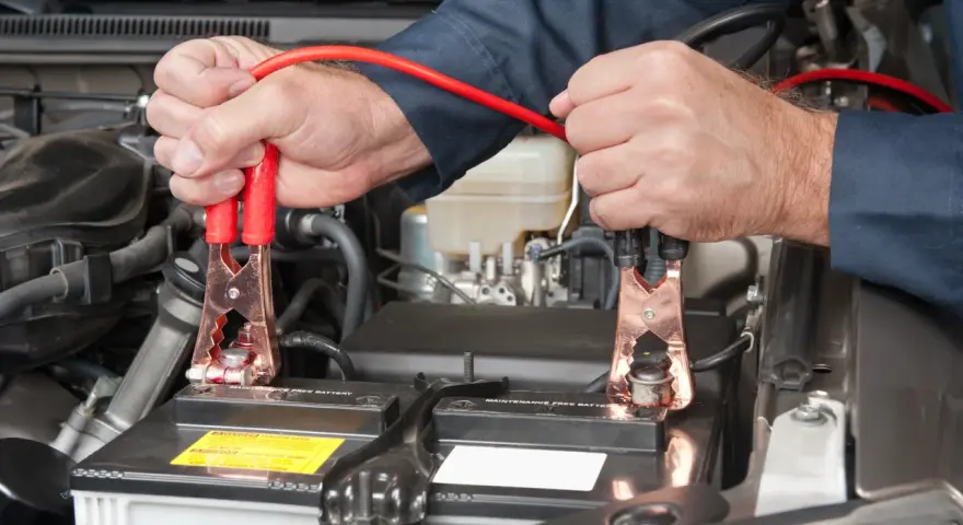 Mains pour recharger batterie voiture avec des câbles de démarrage. Les pinces rouges sont connectées à la batterie.