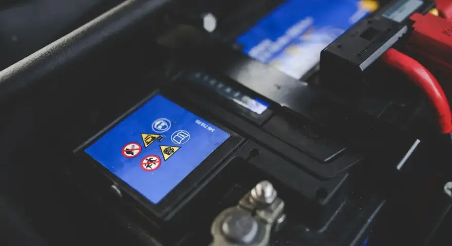 Gros plan sur une batterie de voiture, avec des symboles de sécurité et des câbles rouges. L'image évoque la durée de vie batterie voiture.