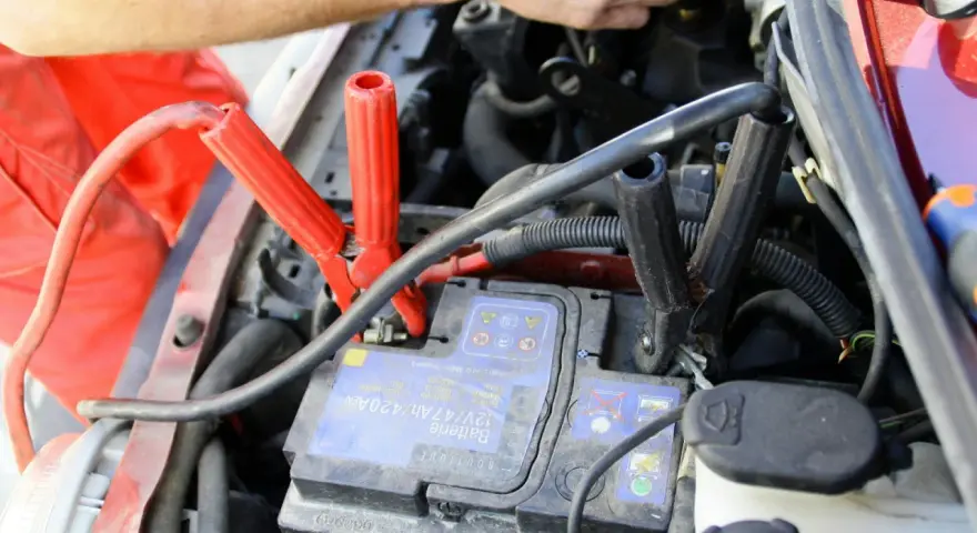Comment utiliser un booster de batterie : des câbles rouges et noirs sont connectés à une batterie de voiture pour la démarrer.