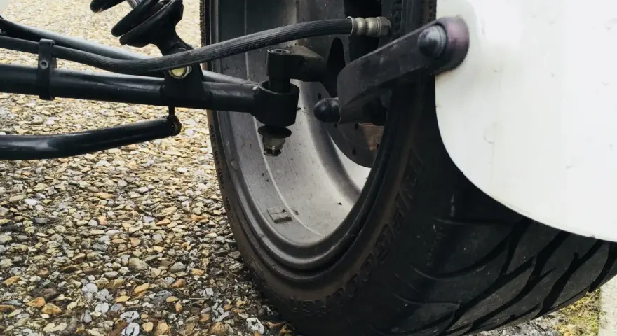 Gros pneu de véhicule sur un chemin de gravier. Le système de suspension et de direction est visible. J'espère que mes pneus font du bruit quand je roule, car cela pourrait indiquer un problème.
