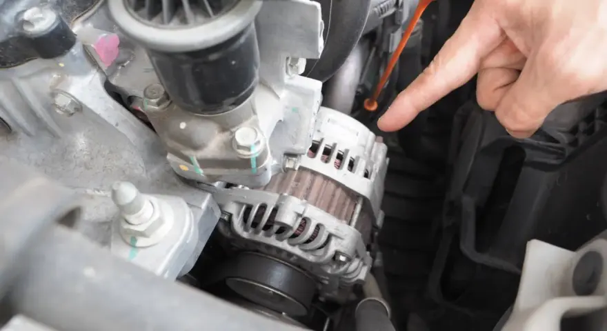 Main d'un mécanicien pointant vers l'alternateur pour tester un régulateur de tension dans un compartiment moteur.