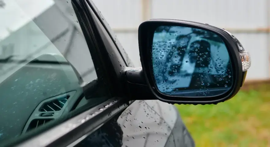 Rétroviseur droit obligatoire depuis quand ? Ce miroir de voiture, couvert de gouttes de pluie, reflète un ciel gris.