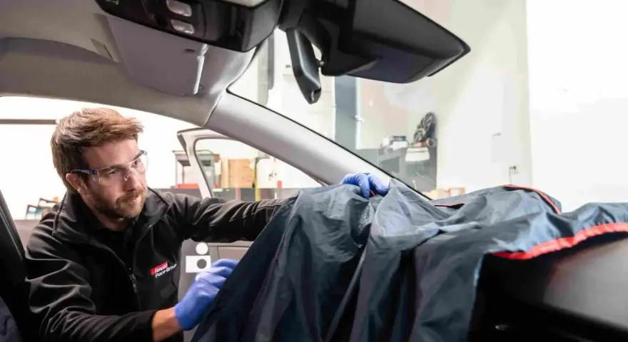 Un technicien en lunettes de protection utilise une housse pour protéger le tableau de bord lors d'une intervention sur la commande de désembuage.