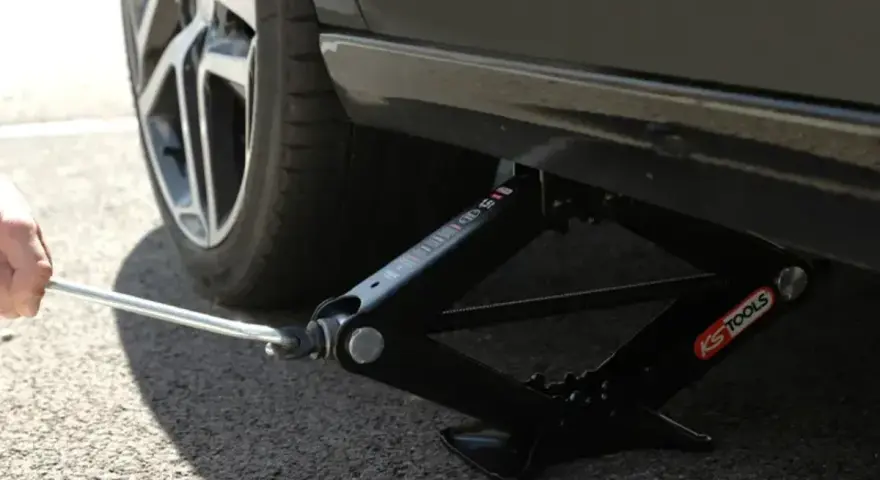 Utilisation d'un cric en ciseaux pour trouver le bon point de levage voiture. La roue est visible.