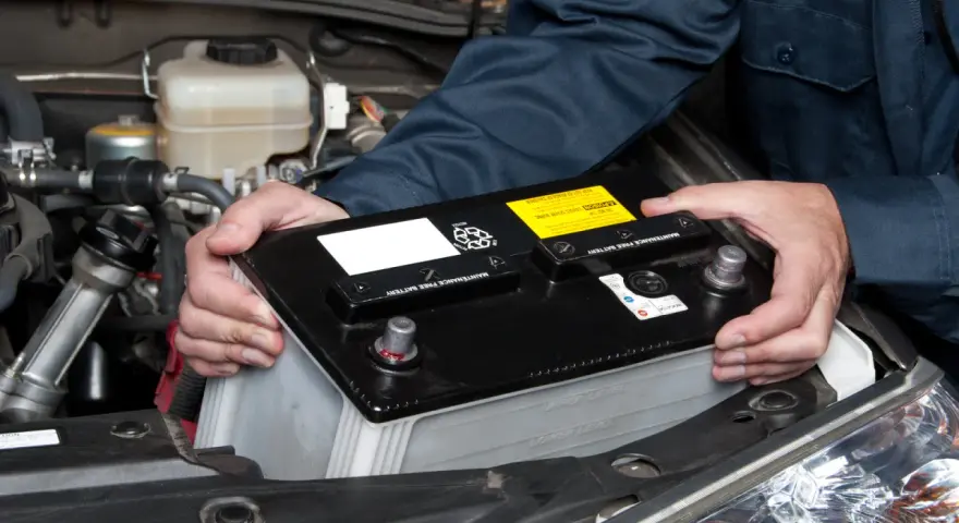 Maintenant, le démontage de la batterie de voiture est en cours. Les mains d'un mécanicien retirent la batterie noire du compartiment moteur.